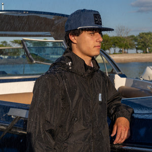 Man in casual wear with a cap and rain jacket, near water.